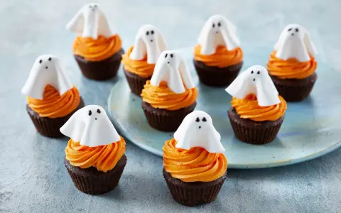 Sju chokladmuffins med orange frosting och vita spökdekorationer. Perfekt att baka till Halloween med barnen!