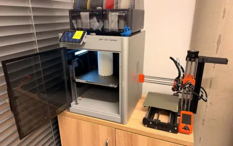 Test drukarki 3D Bambu Lab X1-Carbon z AMS i małą drukarką Prusa Mini obok.