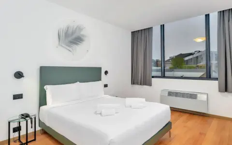 A modern hotel room with a king-size bed, white linens, and a green headboard.