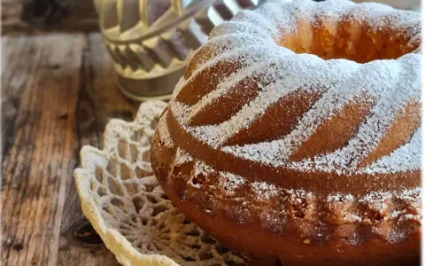 Ciambellone allo yogurt soffice e profumato, cosparso di zucchero a velo su un centrino di pizzo, pronto per essere gustato.