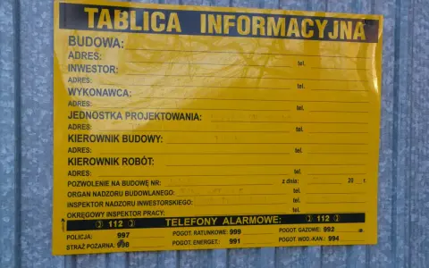 Tablica informacyjna budowy, gdzie można znaleźć dane o pozwoleniach na budowę domu, wykonawcach i numerach alarmowych.