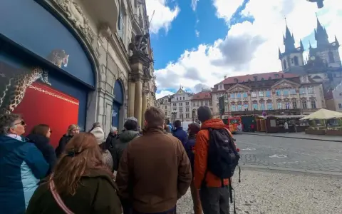 A group of tourists on a prague free walking tour gather on a cobblestone street, with historic buildings and a church in the background.