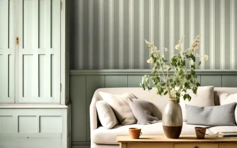 Un salón acogedor con un sofá beige, una mesita de madera y un armario antiguo. El papel para pared con gotele a rayas verdes y blancas crea un ambiente sereno.