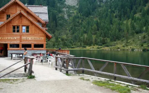 Rifugio sul lago nambino, con tavoli all'aperto e un bosco di conifere sullo sfondo.