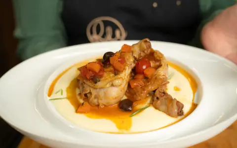 Pollo alla cacciatora succulento su un letto di polenta cremosa, guarnito con pomodorini, olive e carote.