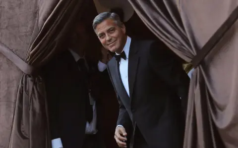 George Clooney, dapper in a tuxedo, emerges from behind velvet curtains. A perfect tix vs suit moment.