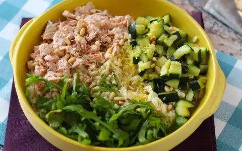 En gul skål med ris, lax, gurka och ruccola. En hälsosam och färgstark måltid.