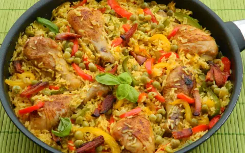 Pyszna paella z kurczakiem, ryżem, papryką i groszkiem w dużej patelni.