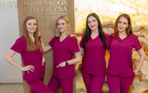 Cztery kobiety w uniformach medycznych stoją obok siebie przed tablicą z napisem "Kosmetologia Estetyczna".