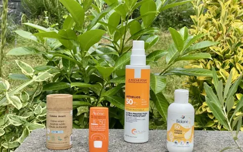 Quatre produits de protection solaire, dont un écran solaire physique, sont alignés sur un muret, entourés de verdure luxuriante.