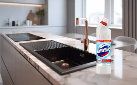 Domestos na zatkany zlew. Nowoczesna kuchnia z czarnym zlewem i złotą baterią, obok butelka Domestos.