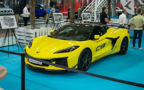 Jaskrawożółty Chevrolet Corvette C8 z czarnym dachem i felgami, prezentowany na niebieskiej podłodze wystawowej.