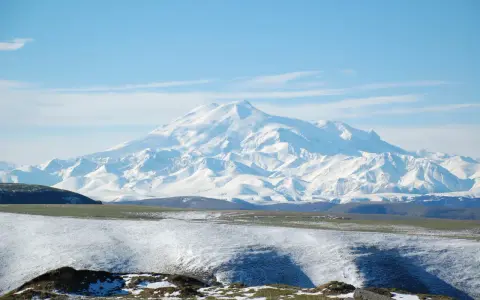 Pokryty śniegiem najwyższy masyw Wielkiego Kaukazu, Elbrus, góruje nad ośnieżonymi wzgórzami i zielonymi dolinami.