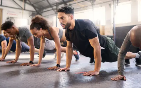 Gruppe trainiert Liegestütze im Fitnessstudio. Ein Mann mit Bart konzentriert sich auf sein ganzheitliches Training.