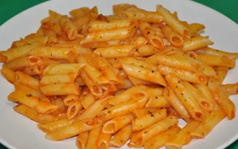 Macarrones penne con salsa de tomate y hierbas en un plato blanco.