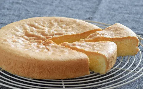 Bizcocho sin gluten esponjoso y dorado, recién cortado en porciones sobre una rejilla.