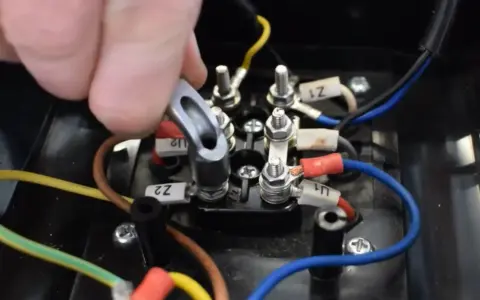 Main d'un technicien manipulant un connecteur sur un bornier électrique. Le moteur électrique chauffe et s'arrête, nécessitant une vérification des connexions.