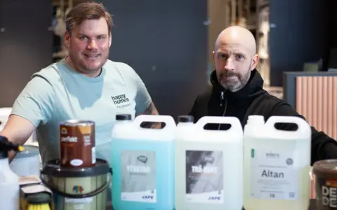 Två män presenterar produkter för att lasera altan. En burk med träolja och flera flaskor med rengöring och skydd.