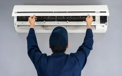 Tecnico con cappellino blu apre il pannello di un climatizzatore per impostare aria fredda.