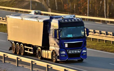 Niebieska ciężarówka z naczepą jedzie autostradą. Kierowca posiada świadectwo kwalifikacji zawodowej, co pozwala mu na bezpieczne przewożenie towarów.