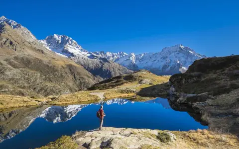 Randonneur contemplant un lac alpin aux reflets parfaits, un paysage grandiose qui pourrait faire partie d'un GR5 itinéraire complet.