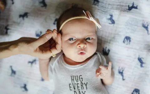 Uroczy 3 tygodniowy noworodek w body z napisem "HUG EVERY DAY", z delikatną opaską na głowie.