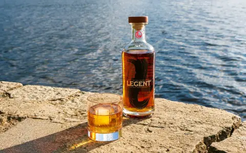 Legent Bourbon Whisky: Ein Glas und eine Flasche stehen auf einem Stein am Wasser. Was ist Bourbon Whisky? Ein Genuss für besondere Momente.