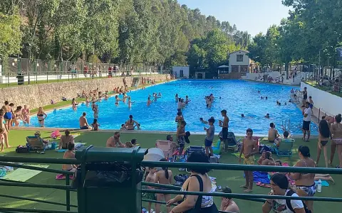 Gente disfrutando de un día soleado en la **piscina segura de la sierra**. Niños y adultos se refrescan en el agua azul, rodeados de árboles y un paisaje montañoso.