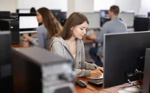 Młoda kobieta, przyszły koder medyczny, skupiona na nauce przy komputerze w sali lekcyjnej.