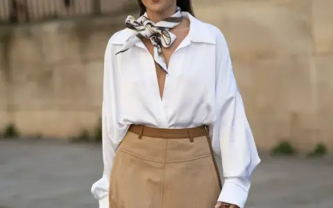 Elegancka biała koszula i beżowa spódnica to świetne **stylizacje jak ukryć brzuch**. Wzorzysty szalik dodaje szyku.