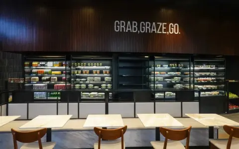Refrigeradores llenos de comidas listas para llevar. El letrero "GRAB, GRAZE, GO" inspira una comida rápida y deliciosa.