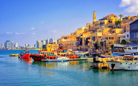Bunte Boote im Hafen von Tel Aviv, mit der historischen Altstadt im Hintergrund und modernen Hochhäusern am Horizont.
