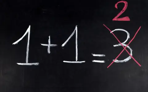 Na czarnej tablicy napisano kredą: 1+1=2. Liczba 3 jest przekreślona, jakby to był trudny egzamin dojrzałości.