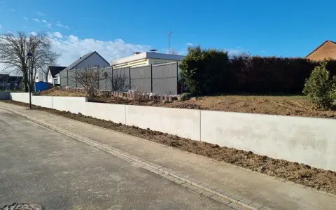 La **fondation mur de soutènement** en béton est prête pour le jardinage. Le ciel bleu et les maisons en arrière-plan annoncent le printemps.