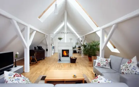 Salon aménagé sous les combles avec cheminée, canapés confortables et poutres apparentes. Le cout d'aménagement combles est bien rentabilisé.