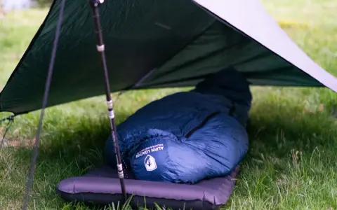 Ein dunkelblauer Kunstfaser-Schlafsack liegt auf einer Isomatte unter einem Tarp. Perfekt für Outdoor-Abenteuer, auch wenn man ihn mal waschen muss.