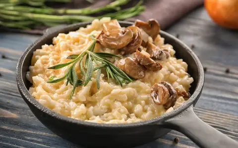 Cremoso arroz redondo risotto con champiñones salteados y romero fresco en sartén de hierro fundido.