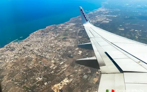 Widok z samolotu Ryanair na wybrzeże i miasto, skrzydło samolotu na pierwszym planie.