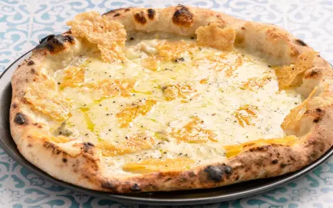 Eine köstliche Pizza quattro formaggi mit geschmolzenem Käse und knusprigem Rand auf einem gemusterten Tisch.