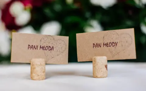 Urocze winietki ślubne z sercami i napisami "Pani Młoda" i "Pan Młody", stojące na korkach od wina.
