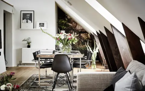 Välkomnande inredd vindsvåning med snedtak, matplats med blommor och konst.