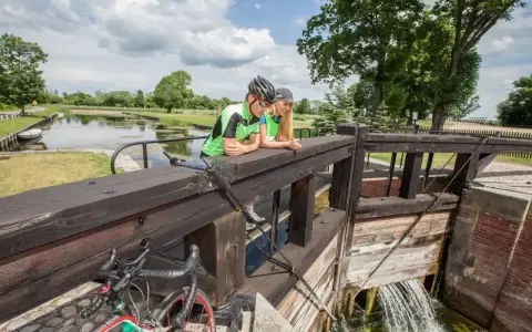Para rowerzystów odpoczywa przy śluzie, podziwiając malownicze **trasy rowerowe Augustów**.