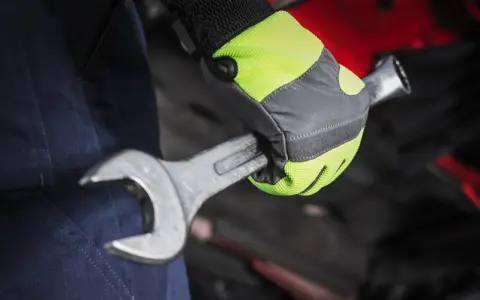 Mano con guante de alta visibilidad, parte de material de protección laboral, sujetando una llave inglesa.