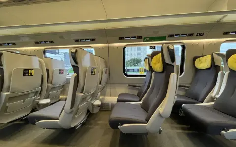 Wnętrze pociągu Pendolino z wygodnymi fotelami w ciemnej tapicerce i żółtymi zagłówkami.