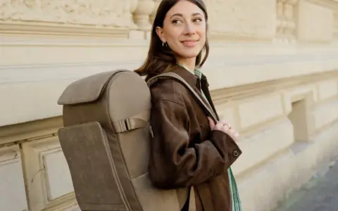 A woman smiles, showcasing the latest backpacks trend with a stylish, taupe backpack.