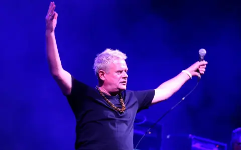 Kazik Staszewski z mikrofonem, ręce w górze, jakby świętował sukces jednej z 20 najlepszych piosenek Kazika.