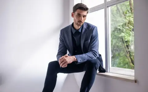 Elegancki mężczyzna w granatowej koszuli i marynarce, zastanawia się, jakie spodnie do niebieskiej koszuli będą najlepsze.