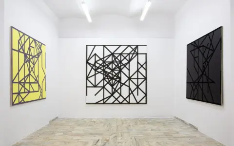 Galeria sztuki z trzema obrazami: żółtym, czarno-białym i czarnym, wszystkie w stylu abstrakcji w malarstwie, z geometrycznymi wzorami.