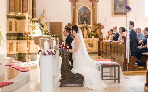 Brautpaar kniet vor dem Altar. Sie heiraten kirchlich, nur ein Partner in der Kirche. Gäste sitzen auf den Bänken.