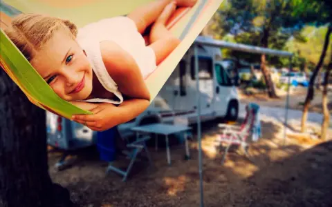 Ein glückliches Mädchen entspannt sich in einer Hängematte auf einem familienfreundlichen Campingplatz. Im Hintergrund stehen Wohnmobile und Campingmöbel.